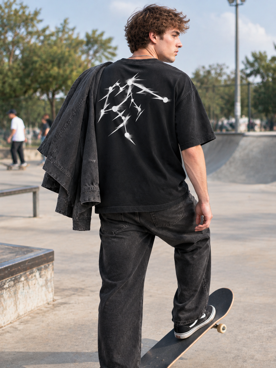 Model resting a foot on a skateboard at a skatepark wearing the black Aquarius constellation graphic tee, back print visible