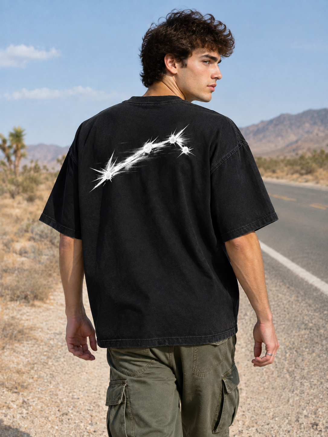 Model walking a desert road wearing the black Aries constellation graphic tee, back print visible